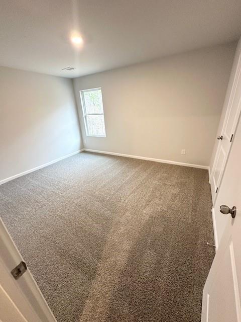 spare room with baseboards and dark colored carpet