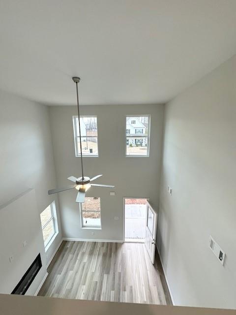 unfurnished living room featuring ceiling fan, light wood-style flooring, a fireplace, a towering ceiling, and baseboards