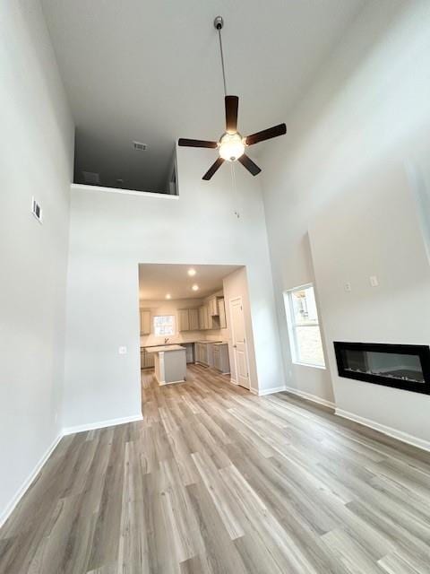 unfurnished living room with light wood-type flooring, a glass covered fireplace, and baseboards