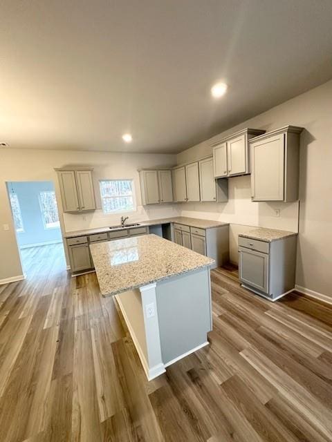 kitchen with dark wood-style floors, a center island, gray cabinets, and light stone countertops