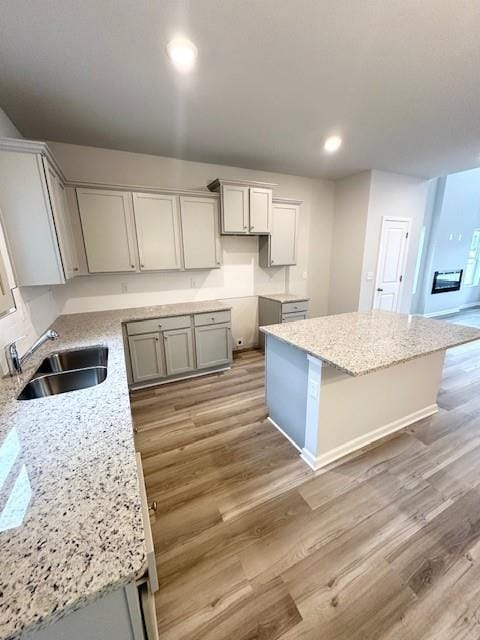 kitchen with light stone counters, a kitchen island, light wood-style flooring, and a sink