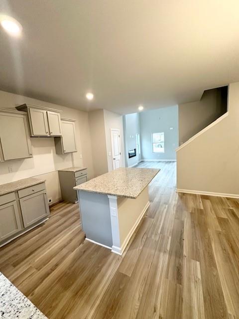 kitchen with light wood finished floors, gray cabinets, a kitchen island, and light stone countertops