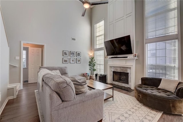 living room with ceiling fan, a fireplace, hardwood / wood-style floors, and a high ceiling