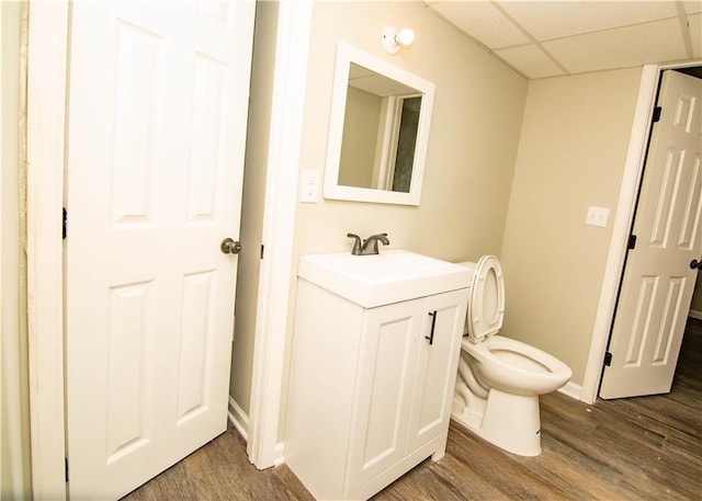 bathroom with hardwood / wood-style flooring, vanity, toilet, and a drop ceiling