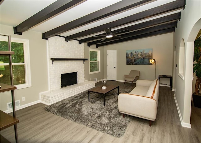 living room with hardwood / wood-style flooring, ceiling fan, a brick fireplace, and beam ceiling