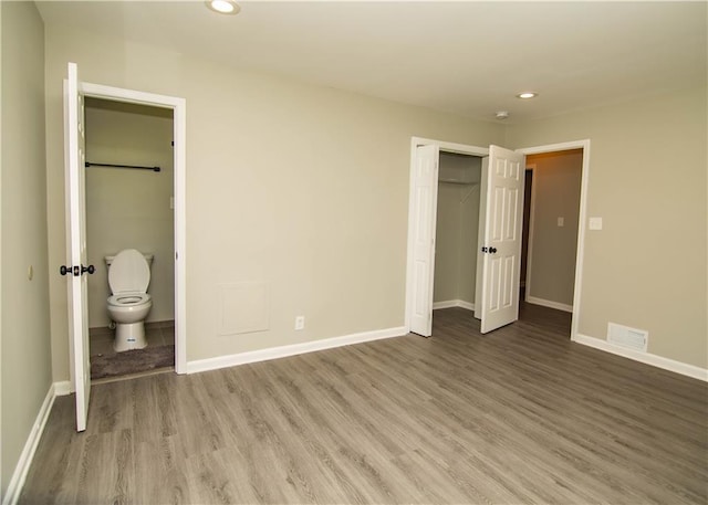 unfurnished bedroom with wood-type flooring, ensuite bathroom, and a closet