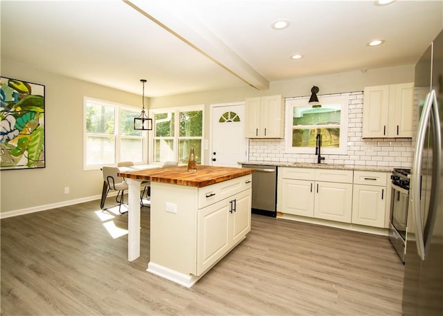 kitchen with appliances with stainless steel finishes, a center island, white cabinets, wood counters, and decorative light fixtures