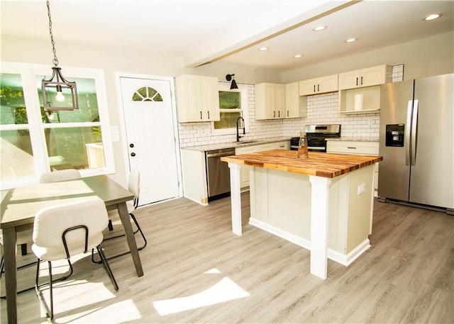 kitchen featuring appliances with stainless steel finishes, pendant lighting, butcher block counters, sink, and a center island