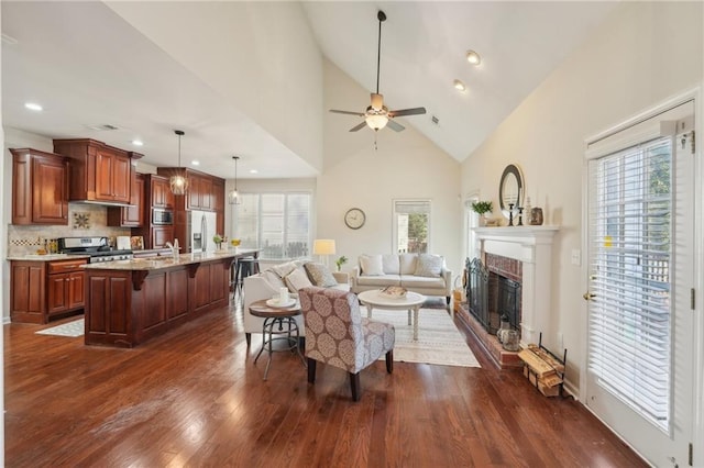 living area with a glass covered fireplace, a ceiling fan, dark wood finished floors, and a wealth of natural light