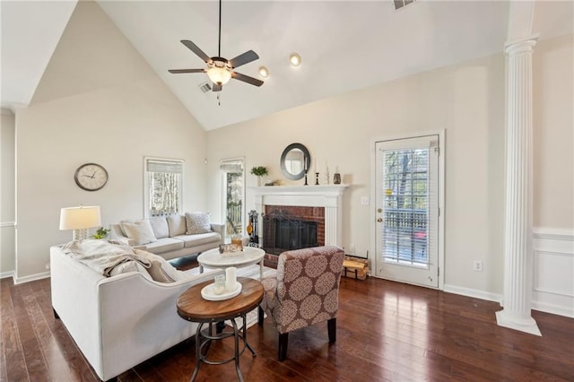 living room featuring high vaulted ceiling, a brick fireplace, ceiling fan, dark wood-style flooring, and ornate columns