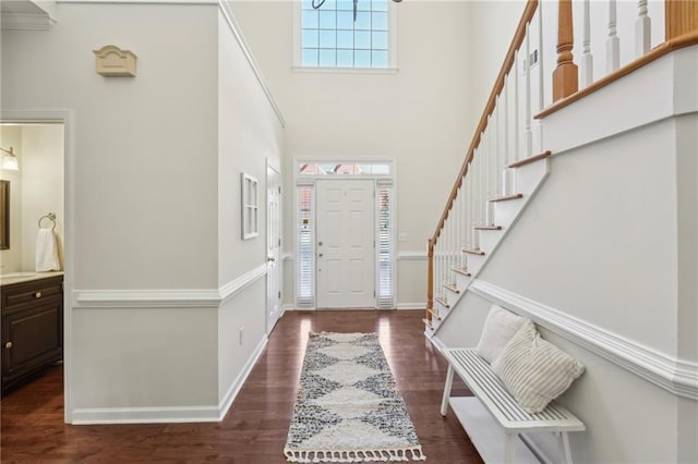 entrance foyer with dark wood-type flooring, stairway, baseboards, and a towering ceiling