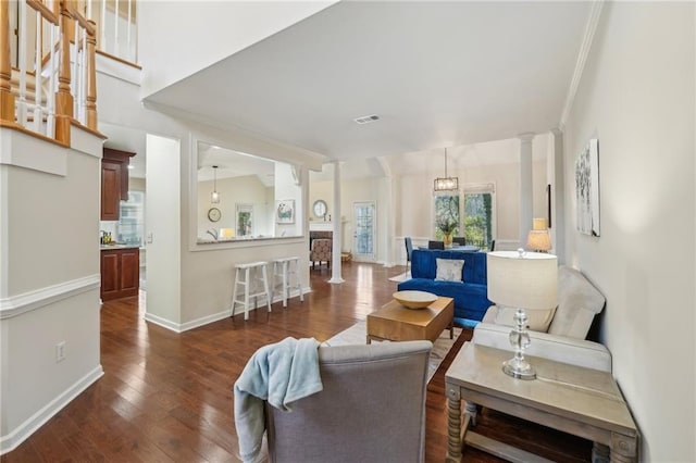 living area featuring visible vents, baseboards, ornamental molding, dark wood-style floors, and ornate columns