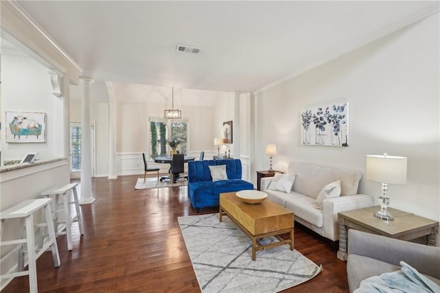 living area featuring wood finished floors, visible vents, decorative columns, ornamental molding, and a chandelier