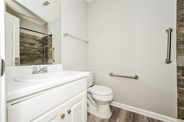 bathroom with vanity, wood finished floors, visible vents, tiled shower, and toilet