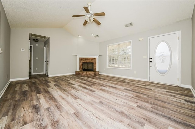 unfurnished living room featuring wood finished floors, visible vents, lofted ceiling, ceiling fan, and a stone fireplace