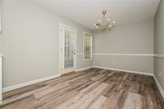 empty room featuring an inviting chandelier, wood finished floors, baseboards, and a textured ceiling