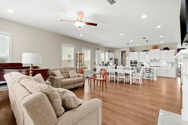 living room featuring ceiling fan, light wood-type flooring, and a healthy amount of sunlight