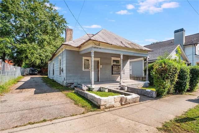 view of front of property with a chimney, a porch, driveway, and fence