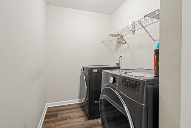 washroom featuring baseboards, wood finished floors, laundry area, and washing machine and clothes dryer