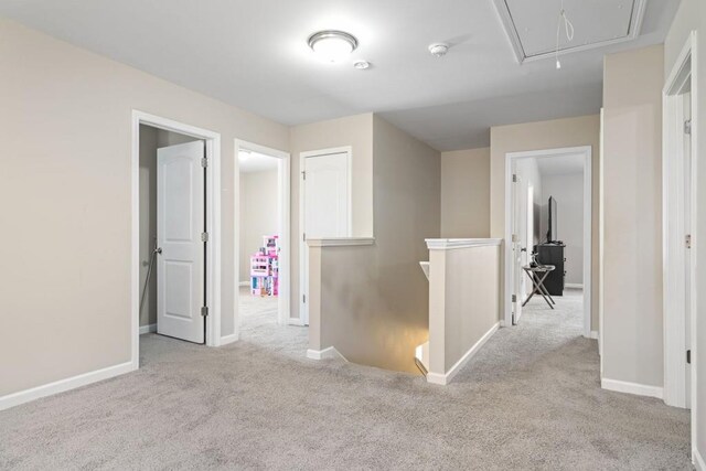 corridor with an upstairs landing, attic access, baseboards, and carpet floors