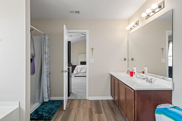 ensuite bathroom with visible vents, connected bathroom, a shower with shower curtain, wood finished floors, and a sink