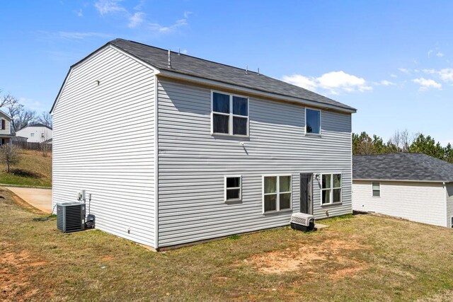 rear view of property with central air condition unit and a yard