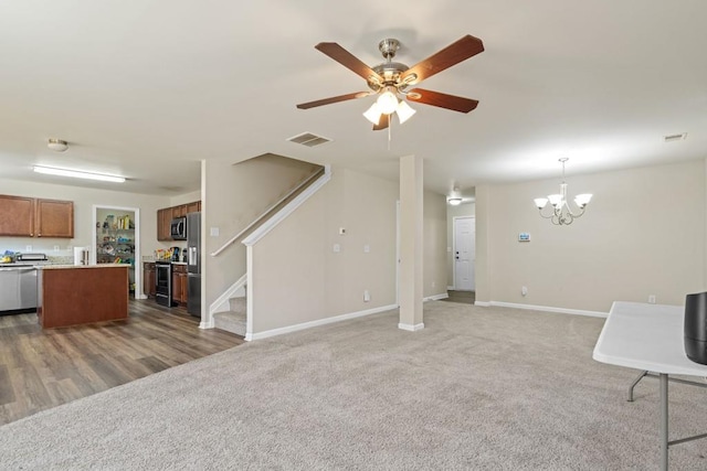 unfurnished living room with baseboards, visible vents, stairs, carpet flooring, and ceiling fan with notable chandelier