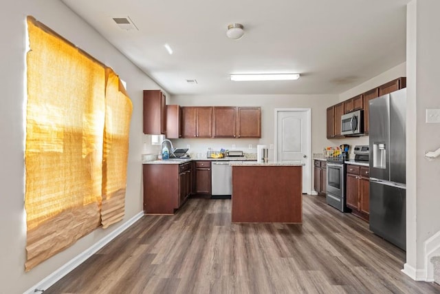 kitchen featuring a kitchen island, light countertops, appliances with stainless steel finishes, dark wood-style floors, and a sink