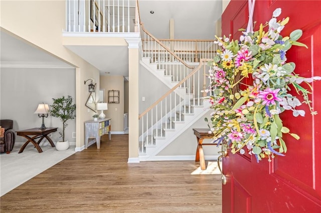 foyer featuring baseboards, stairway, ornamental molding, wood finished floors, and a high ceiling