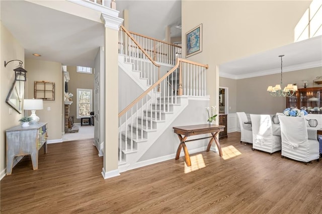 staircase with crown molding, a notable chandelier, a towering ceiling, and wood finished floors