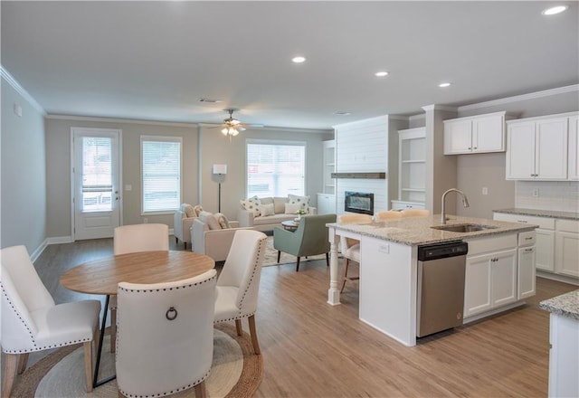 kitchen featuring white cabinets, ornamental molding, a center island with sink, dishwasher, and light stone countertops