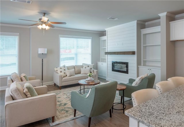 living room featuring a large fireplace, light hardwood / wood-style flooring, built in features, ceiling fan, and ornamental molding