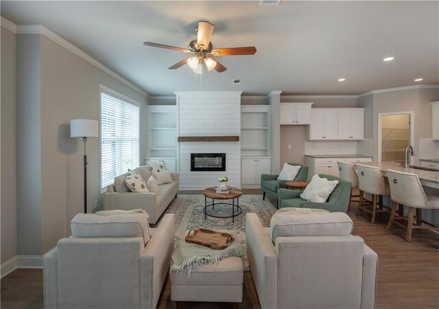 living room featuring ornamental molding, dark hardwood / wood-style flooring, ceiling fan, and a large fireplace