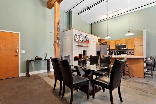 dining room with a towering ceiling, concrete floors, baseboards, and track lighting