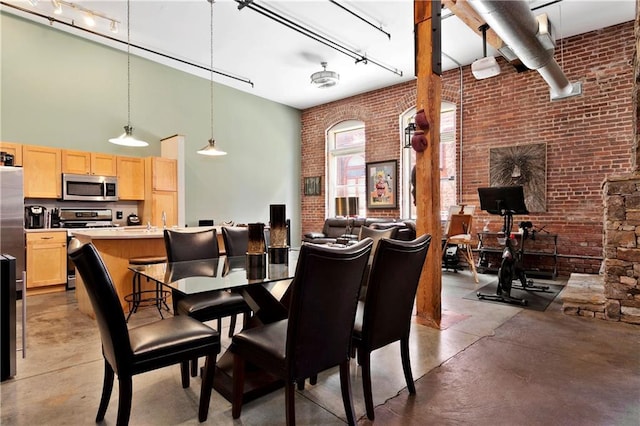 dining room featuring brick wall, a high ceiling, and concrete floors