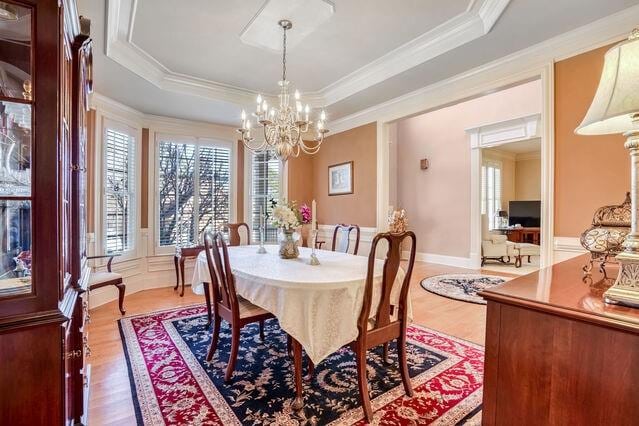 dining space with a raised ceiling, crown molding, wood-type flooring, and an inviting chandelier