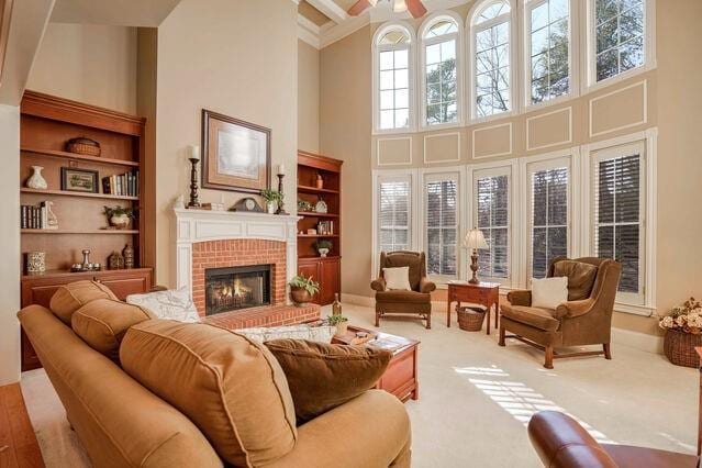 living room with ceiling fan, carpet floors, a high ceiling, and a brick fireplace