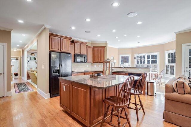 kitchen featuring light stone countertops, light hardwood / wood-style floors, a breakfast bar area, a kitchen island, and black appliances