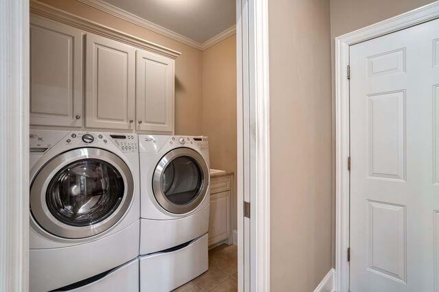 laundry area with washer and clothes dryer, cabinets, light tile patterned floors, and ornamental molding