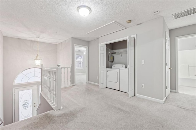 corridor with light carpet, a textured ceiling, and washing machine and clothes dryer