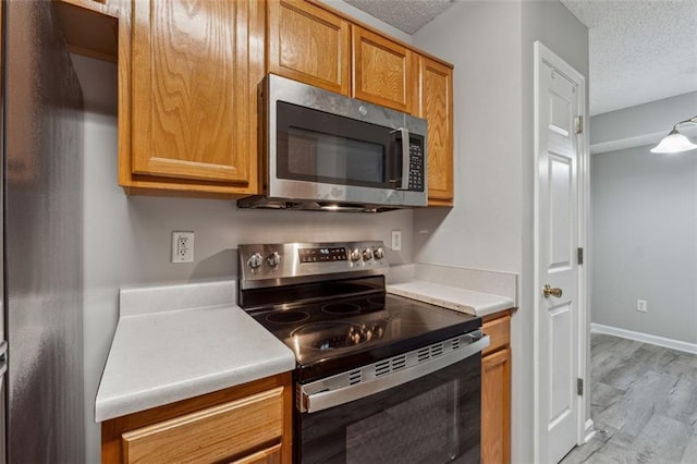 kitchen with stainless steel appliances, a textured ceiling, and light wood-type flooring