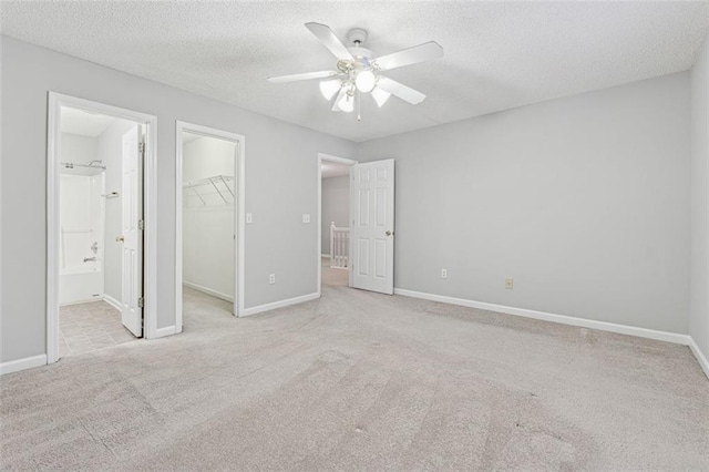 unfurnished bedroom featuring light carpet, ensuite bathroom, a walk in closet, ceiling fan, and a closet