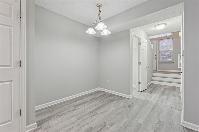 unfurnished dining area with light hardwood / wood-style flooring, a textured ceiling, and a notable chandelier