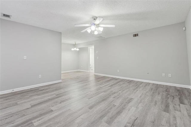 spare room with a textured ceiling, ceiling fan with notable chandelier, and light wood-type flooring