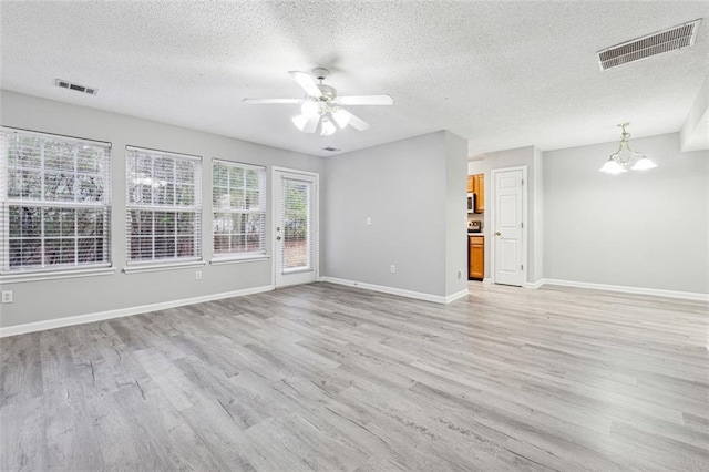 unfurnished living room with a textured ceiling, ceiling fan with notable chandelier, and light hardwood / wood-style flooring