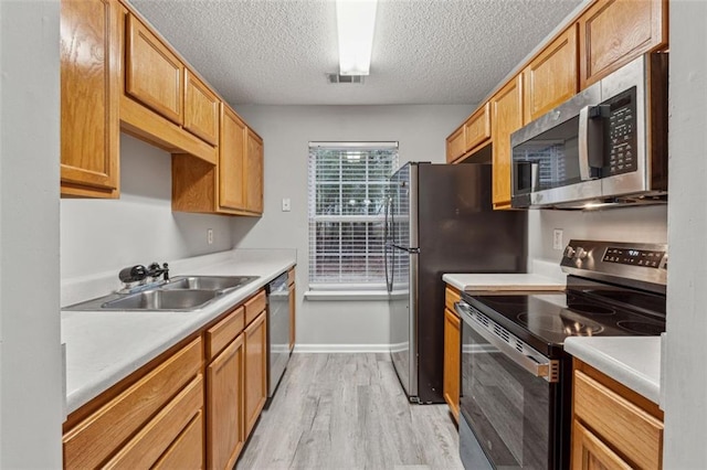 kitchen with a textured ceiling, sink, light wood-type flooring, and stainless steel appliances