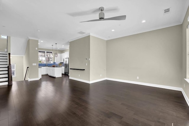 unfurnished living room with visible vents, ornamental molding, a ceiling fan, baseboards, and dark wood-style flooring