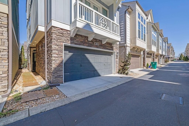 view of property exterior with a residential view, stone siding, driveway, and an attached garage