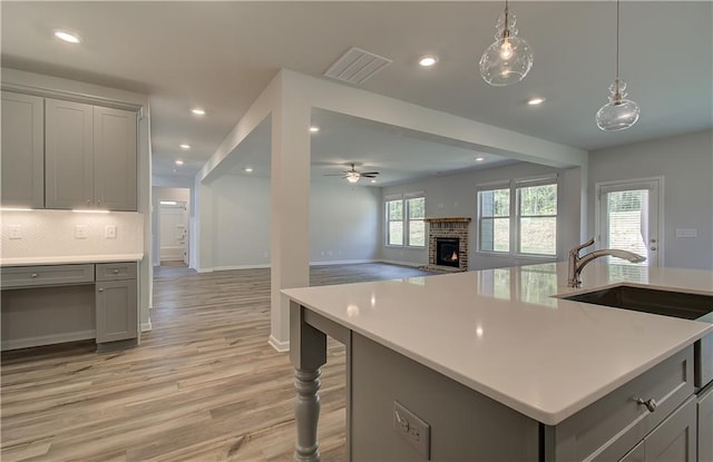 2516 Cadenza Cir, Dacula, GA 30019 - kitchen with gray cabinetry, a brick fireplace, light countertops, light wood-type flooring, and recessed lighting