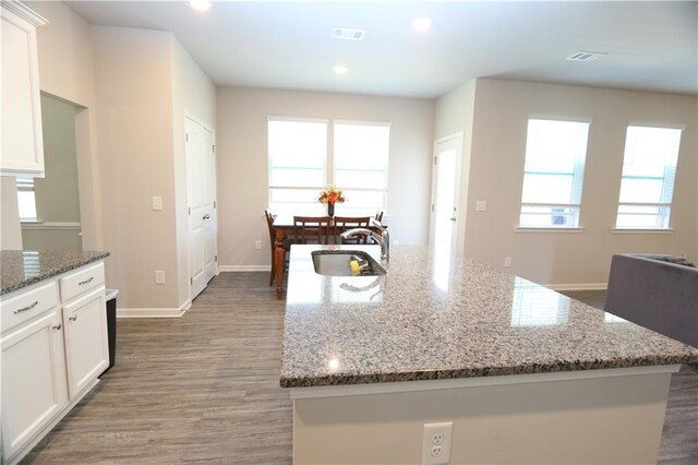 kitchen with a kitchen island with sink, sink, dark stone countertops, and white cabinetry